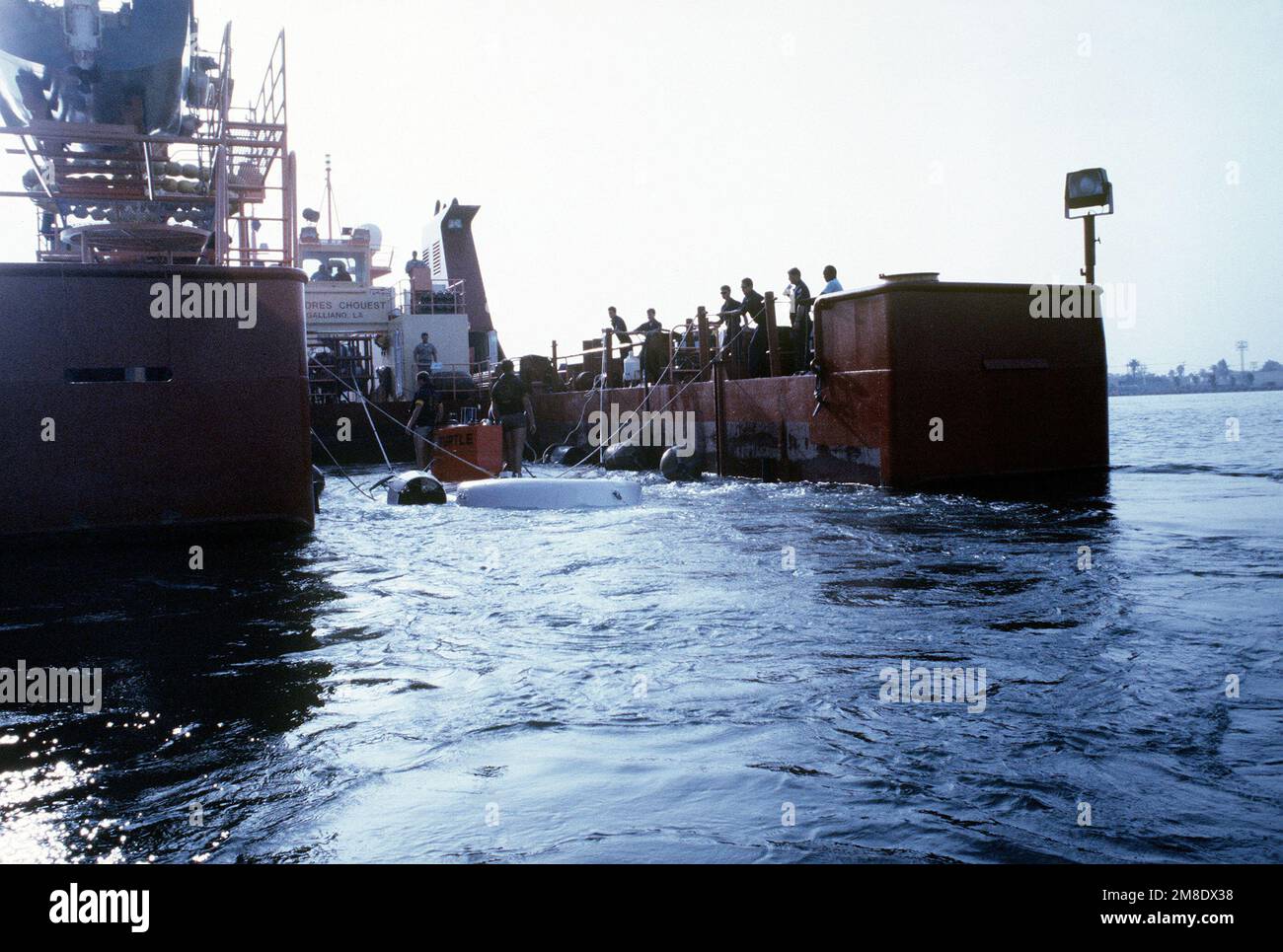 Les membres d'équipage à bord du navire de soutien civil DOLORES CHOUEST se tiennent sur les lignes d'amarrage comme les États-Unis La TORTUE marine (DSV 3) s'attache dans le puits d'amarrage du navire pendant les essais en mer au large de l'île du Nord. Base : San Diego Bay État : Californie (CA) pays : États-Unis d'Amérique (USA) Banque D'Images