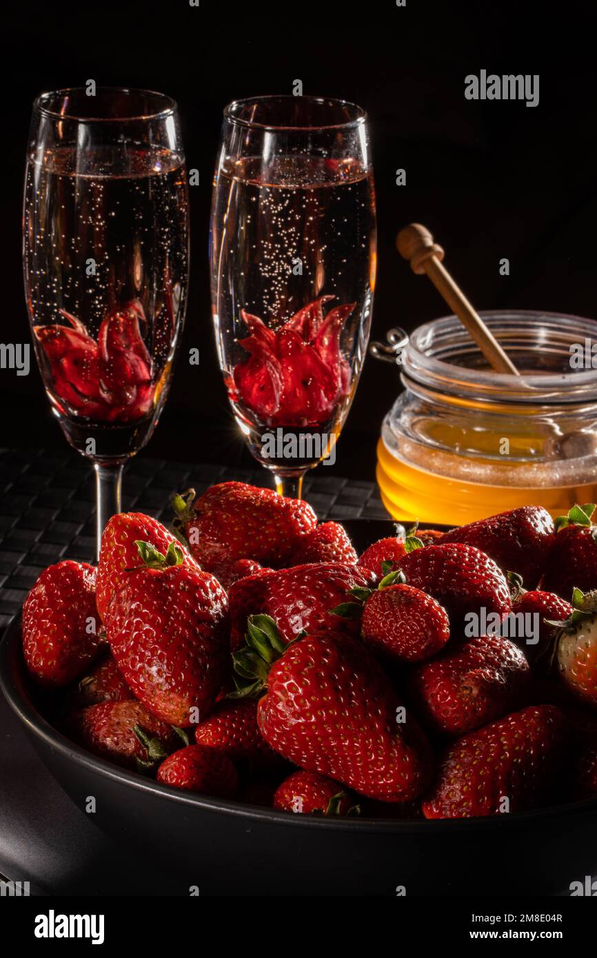 Une scène romantique de champagne, de fleurs d'hibiscus, de fraises et de miel dans une scène sombre. Idéal pour le menu, le site Web ou la publication. Banque D'Images