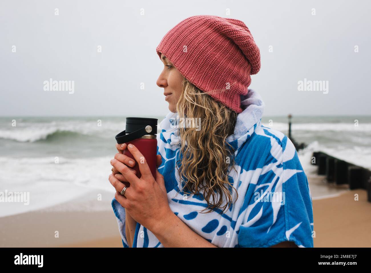 Femme tenant une boisson chaude après avoir nagé d'eau froide dans la mer Banque D'Images