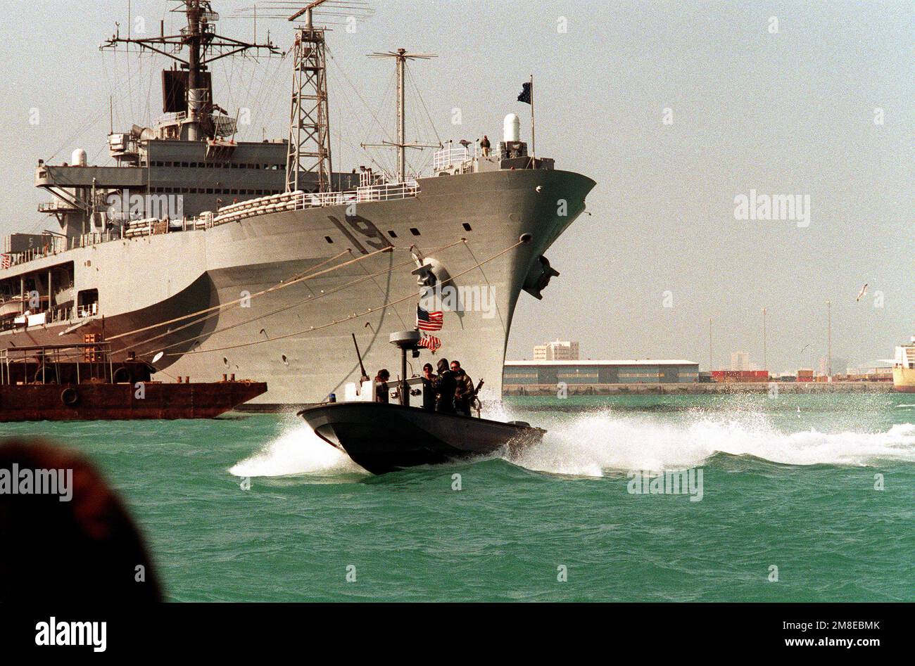 Le personnel de sécurité de la Garde côtière dans un véhicule utilitaire Sea Raider passe devant l'arc du navire de commandement amphibie USS BLUE RIDGE (LCC-19) pendant qu'il patrouille dans le port pendant l'opération Desert Shield. Objet opération/série : BOUCLIER DU DÉSERT pays : Bahreïn (BHR) Banque D'Images