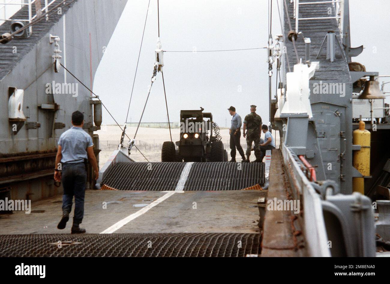 Un membre de l'équipage se tient à votre disposition pour guider le conducteur d'un chariot élévateur à fourche lorsqu'il monte à bord du navire-citerne USS MANITOWOC (LST-1180). Le navire transporte du personnel et de l'équipement du corps des Marines en Arabie saoudite à l'appui de l'opération Desert Shield. Sujet opération/série: DESERT SHIELD État: Caroline du Nord (NC) pays: États-Unis d'Amérique (USA) Banque D'Images