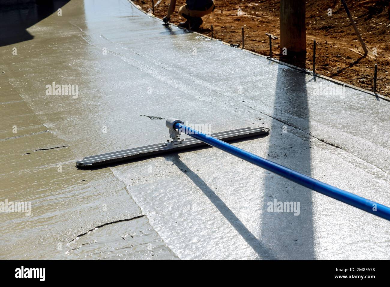 Le travailleur tient une truelle de Fresno en acier et lisse le trottoir nouvellement versé sur le béton humide où la construction a lieu Banque D'Images