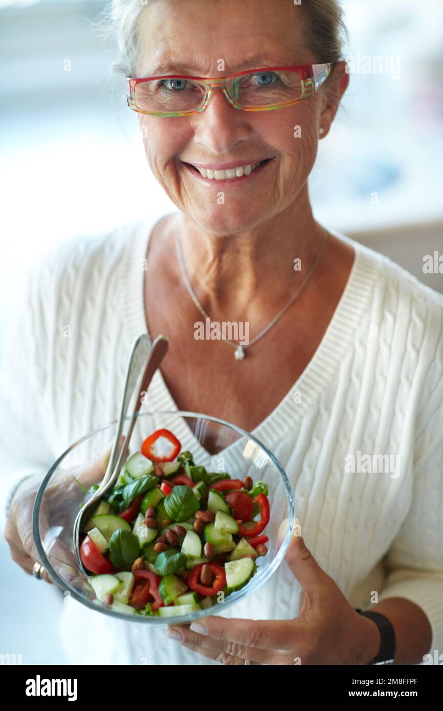 Délicieux et frais. Femme âgée en bonne santé tenant un bol en verre rempli de salade fraîche. Banque D'Images