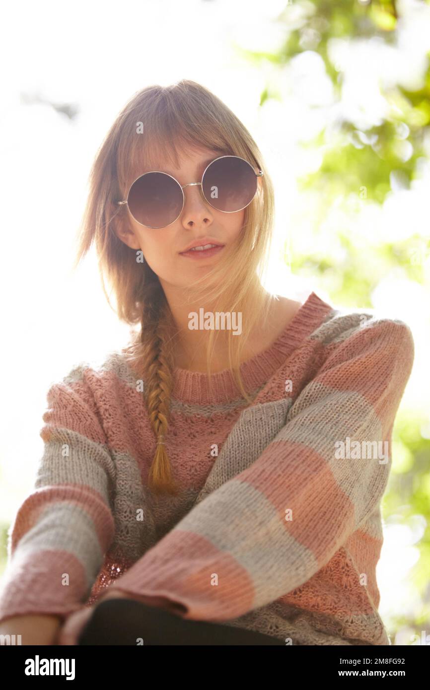Profitez de la douce brise estivale. une jeune femme attrayante portant des lunettes de soleil et assise à l'extérieur. Banque D'Images