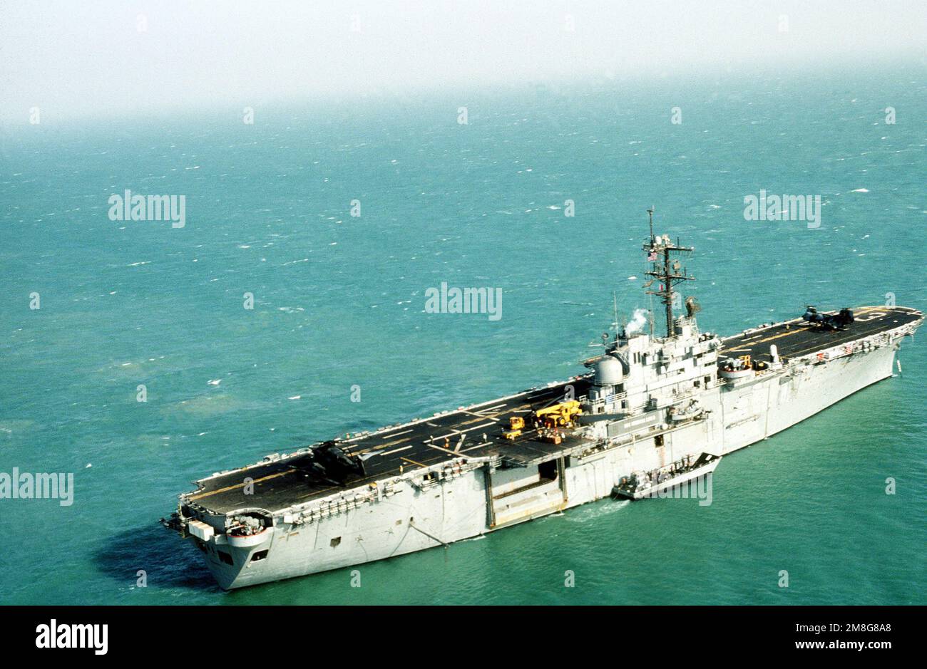 Une vue à tribord du navire d'assaut amphibie USS OKINAWA (LPH-3) amarré dans le golfe, avec un bateau d'atterrissage mécanisé tiré le long. Les membres d'équipage d'OKINAWA et d'autres navires participent à l'exercice Eager Mace 92-1, le premier important exercice de service combiné États-Unis/Koweït depuis la fin de l'opération Desert Storm. Objet opération/série: EAGER MACE 92-1DESERT PAYS DE LA TEMPÊTE: Le golfe Persique Banque D'Images