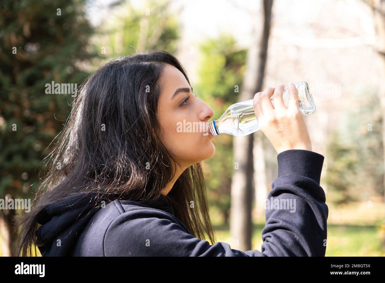 Profil de vue latérale de la jeune femme de l'eau potable. Contenant une bouteille en verre. Jogging, course, faire une pause. Activités de plein air en automne. Habitudes de vie saines. Banque D'Images