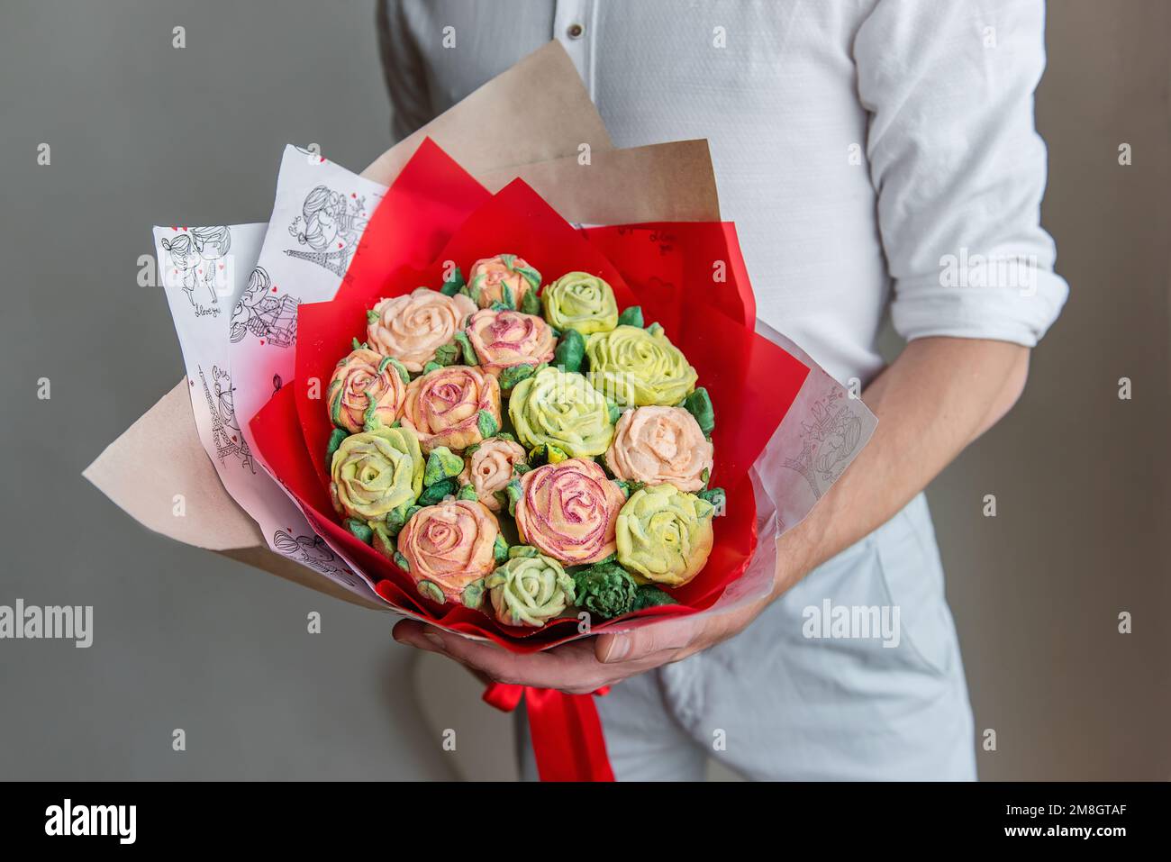 Homme sans visage tient un bouquet de fleurs douces de guimauve dans ses mains. Un cadeau dans un emballage rouge avec des roses de sucre délicates sur un fond clair. Petit Banque D'Images