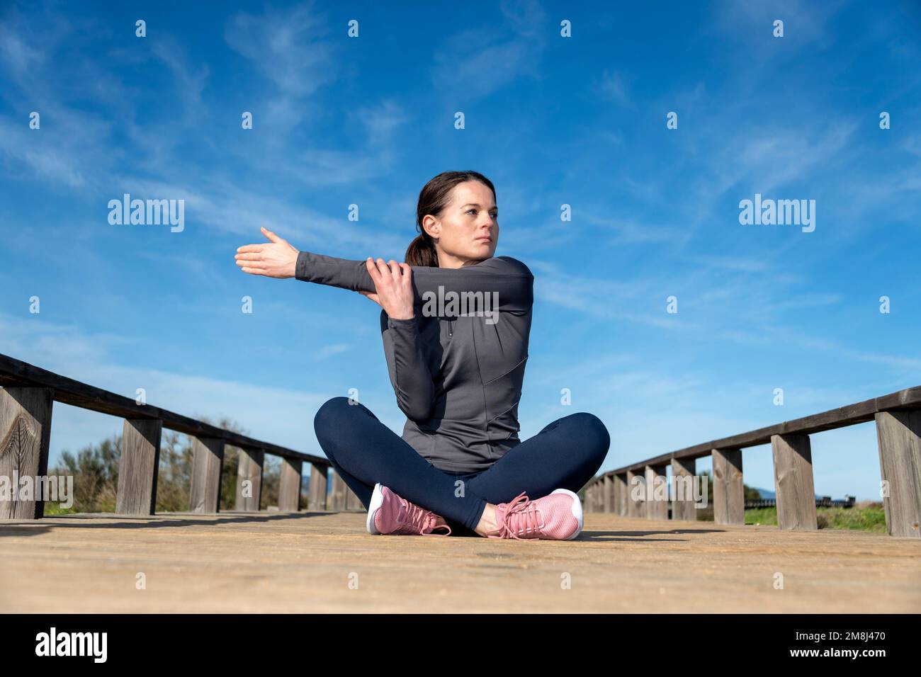 Femme sportive assise à jambes croisées faisant un exercice d'échauffement d'étirement d'épaule avant de s'entraîner à l'extérieur. Banque D'Images