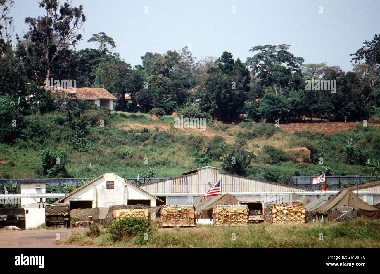Des palettes de fournitures de secours sont placées sur la rampe de l'aéroport international d'Entebbe, en attente du transport aérien vers Goma, Zaïre. Les drapeaux américains survolent les tentes utilisées par le personnel militaire des États-Unis pour soutenir l'effort humanitaire en faveur des réfugiés de la guerre civile rwandaise. Objet opération/série: BASE D'ESPOIR DE SOUTIEN: Entebbe pays: Ouganda (UGA) Banque D'Images