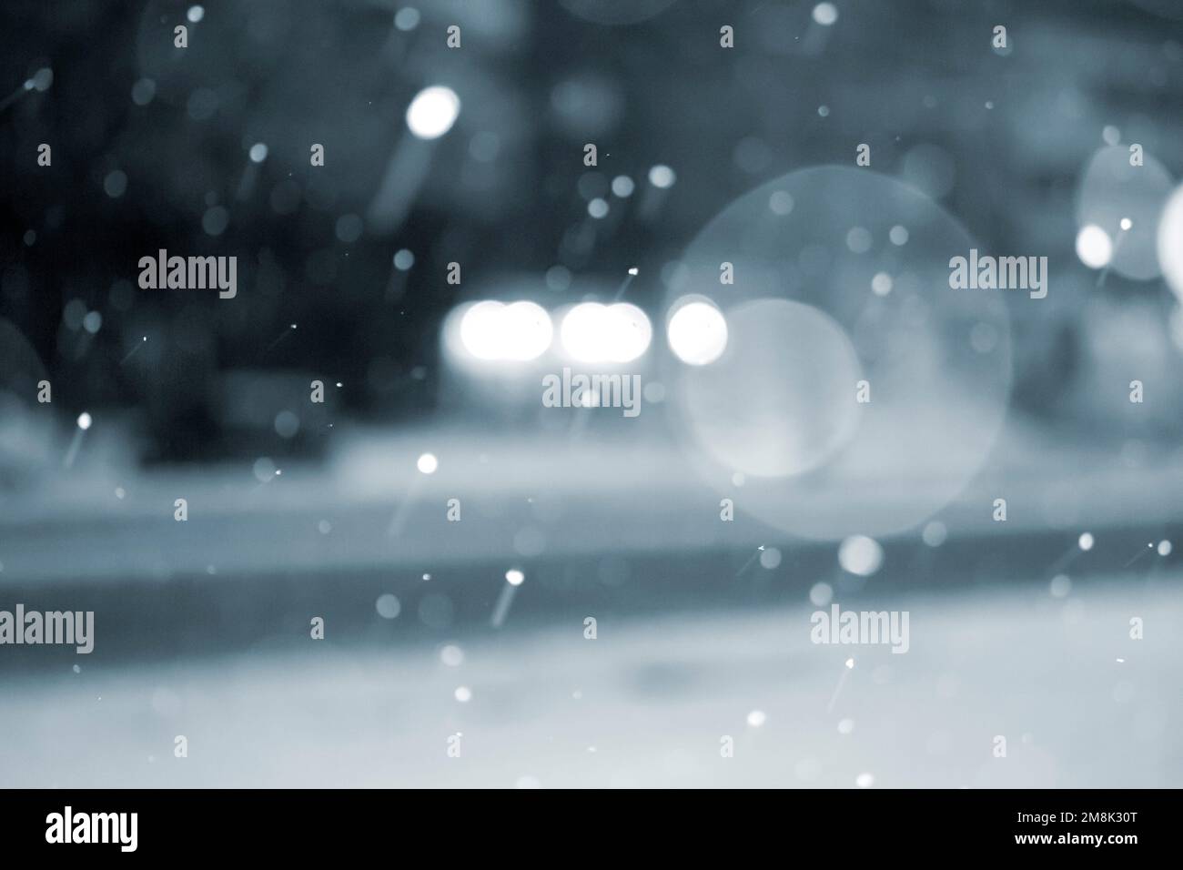 Arrière-plan flou. Voitures roulant sur la route en ville pendant la neige la nuit d'hiver. Taches de bokeh floues. Éclairage de rue, lanternes, lumière de phares lumineux. Décor hivernal. Couleur bleue Banque D'Images