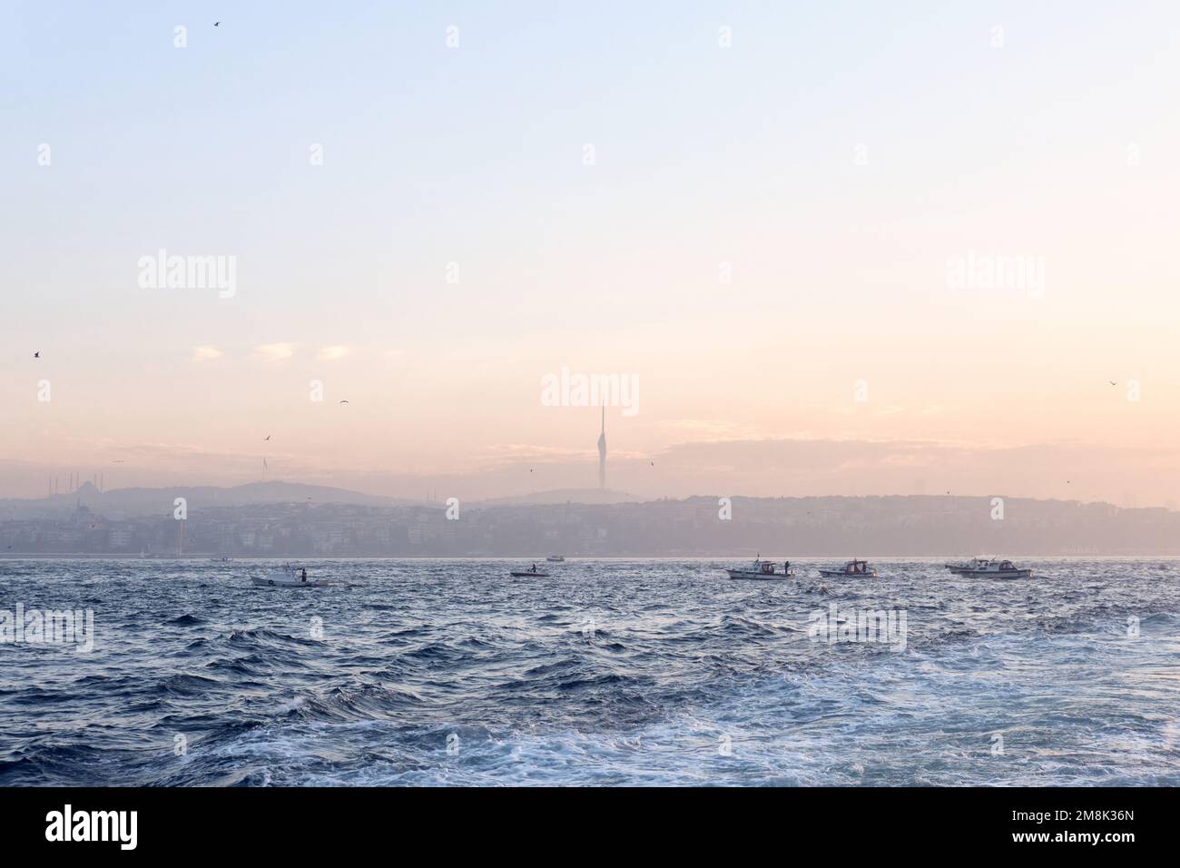 Istanbul, Turquie - janvier 2023 : bateaux de pêche pêchant sur le Bosphore de la mer de Marmara au lever du soleil derrière les gratte-ciel d'Anatolie avec la Tour Camlica Banque D'Images