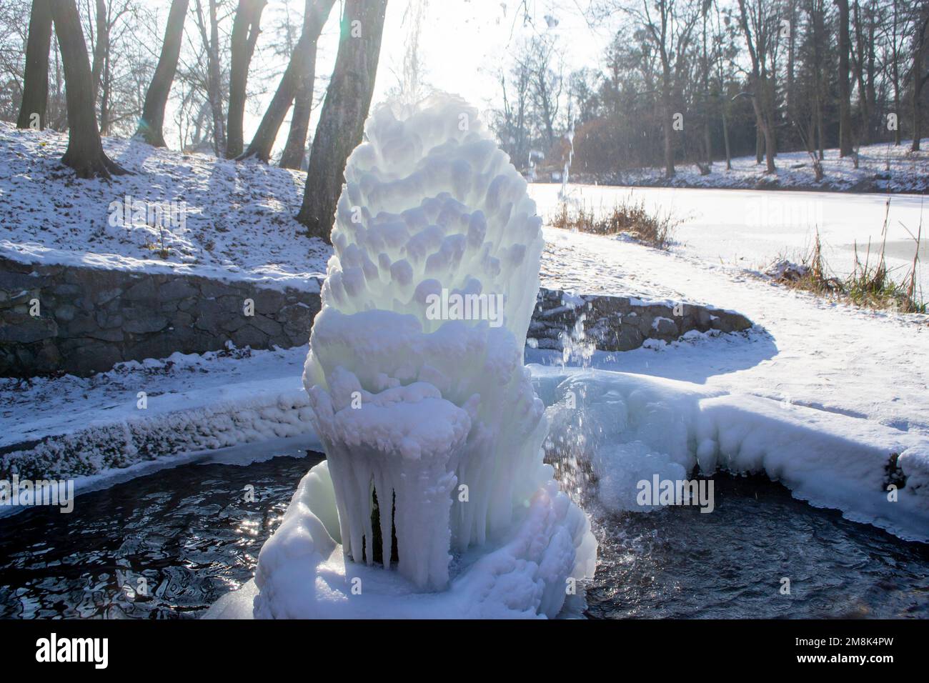 Fontaine glacée dans le parc par une journée ensoleillée en hiver. Fontaine avec eau gelée. Un jet d'eau d'une fontaine qui a glacé dans le froid. Arrière-plan couvert de glace et de neige dans le parc le jour Banque D'Images