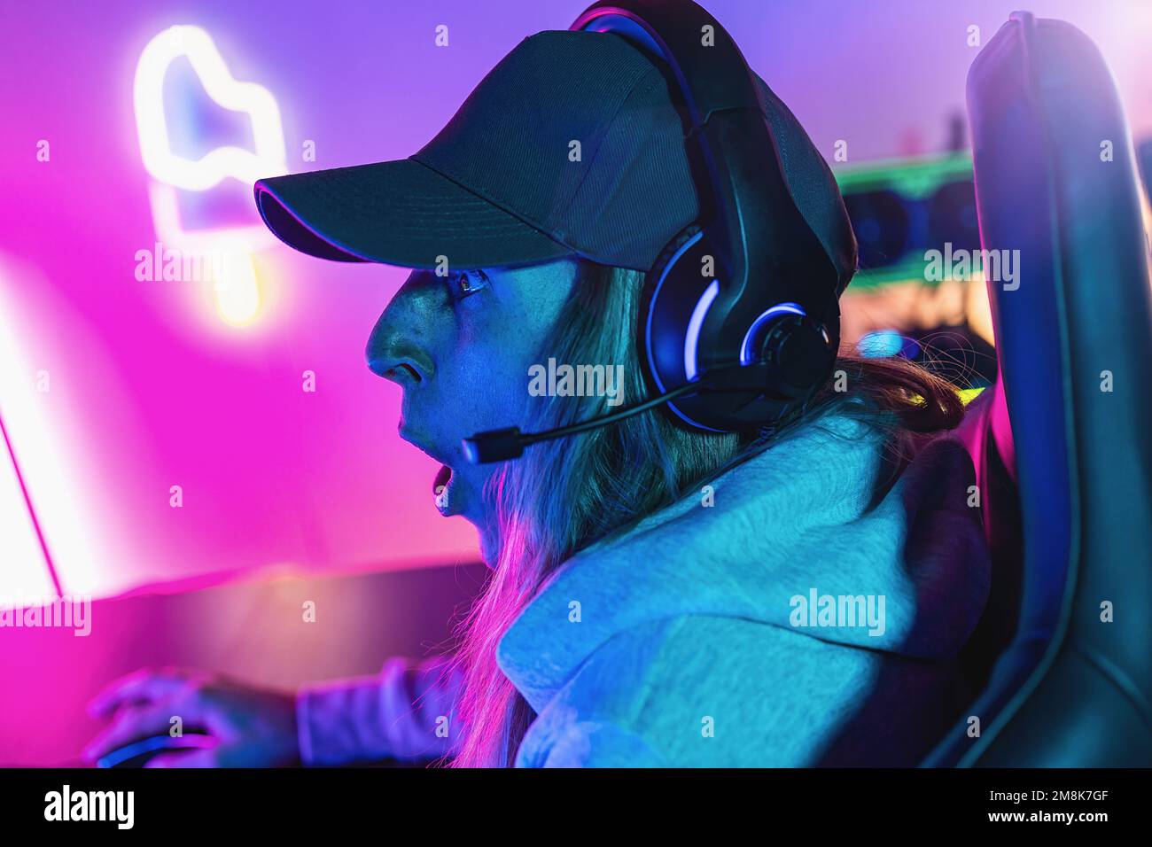 Une femme stupéfait joue à un jeu vidéo en ligne sur son ordinateur personnel. Salle éclairée par des néons dans un style arcade rétro. Internet Cyber e-Sport en ligne Banque D'Images