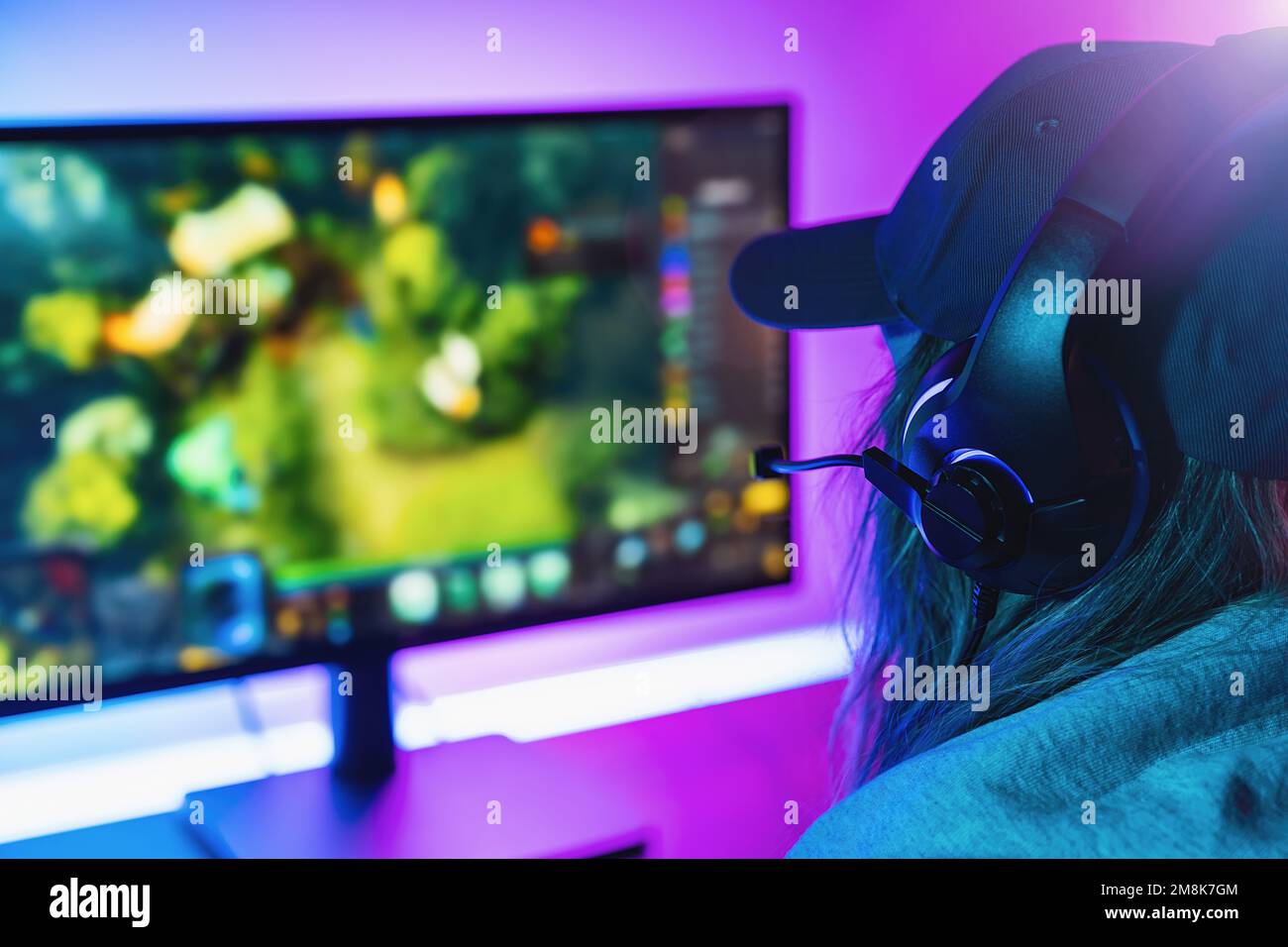 Femme joueur joue stratégie jeu vidéo en ligne sur son ordinateur personnel. Salle éclairée par des néons dans un style arcade rétro. Internet Cyber e-Sport en ligne Banque D'Images