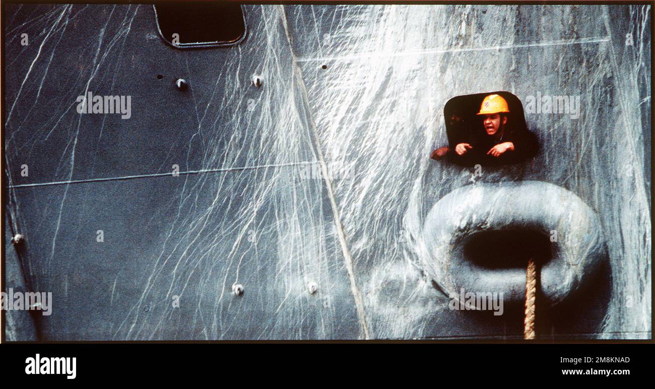 Photographe militaire de l'année gagnant 1996 titre: Trou de port Catégorie: Picturale lieu: Troisième place brève Description: Une petite photo d'un marin dans un casque de sécurité jaune est imposée sur l'extérieur d'un grand navire de marine Date exacte prise de vue inconnue. Pays : inconnu Banque D'Images