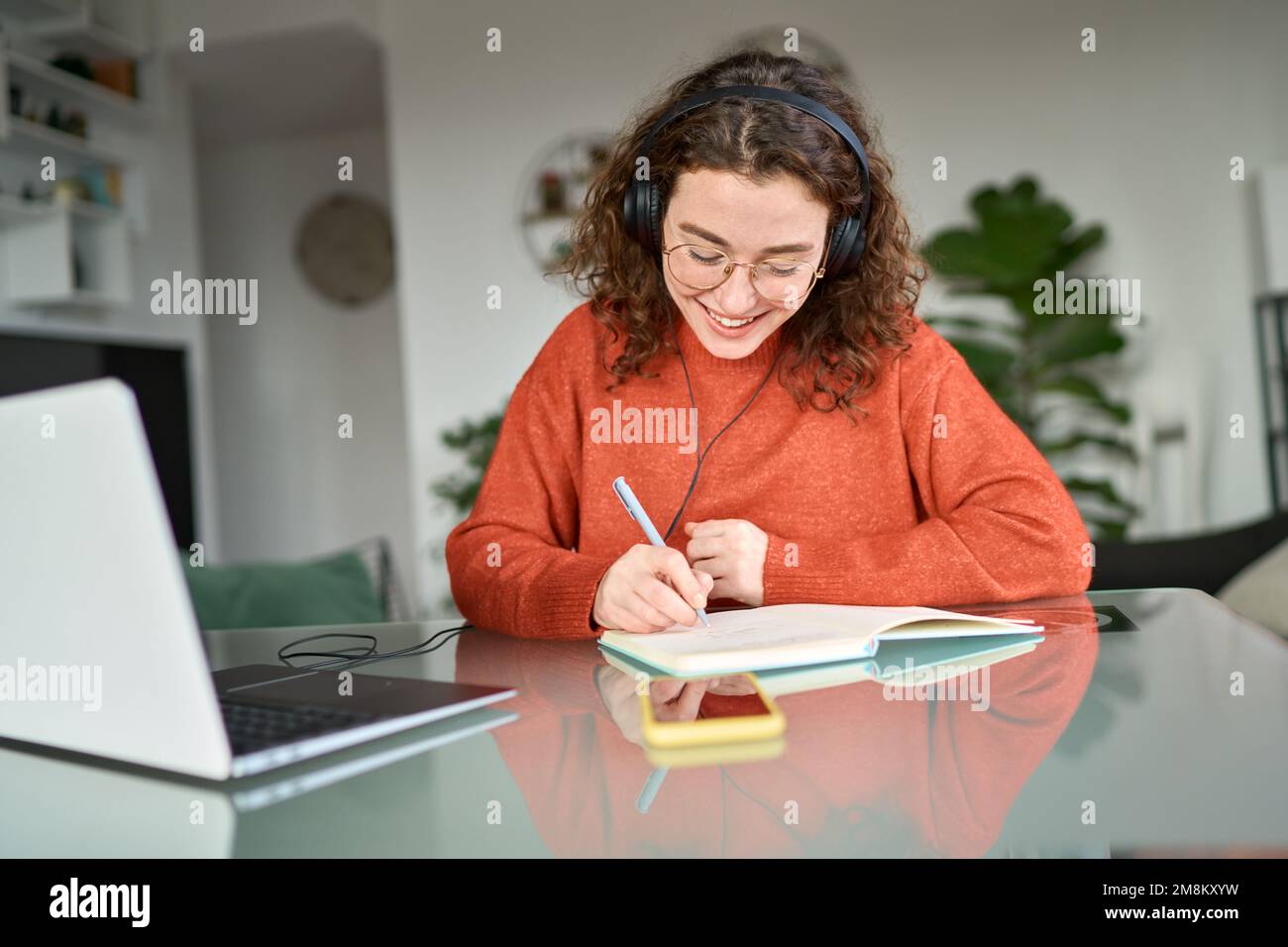 Bonne fille étudiante portant des écouteurs en utilisant l'apprentissage en ligne d'ordinateur portable, l'écriture. Banque D'Images