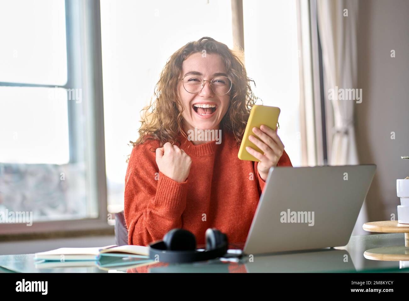 Jeune femme heureuse et excitée étudiante tenant un téléphone mobile célébrant la victoire. Banque D'Images