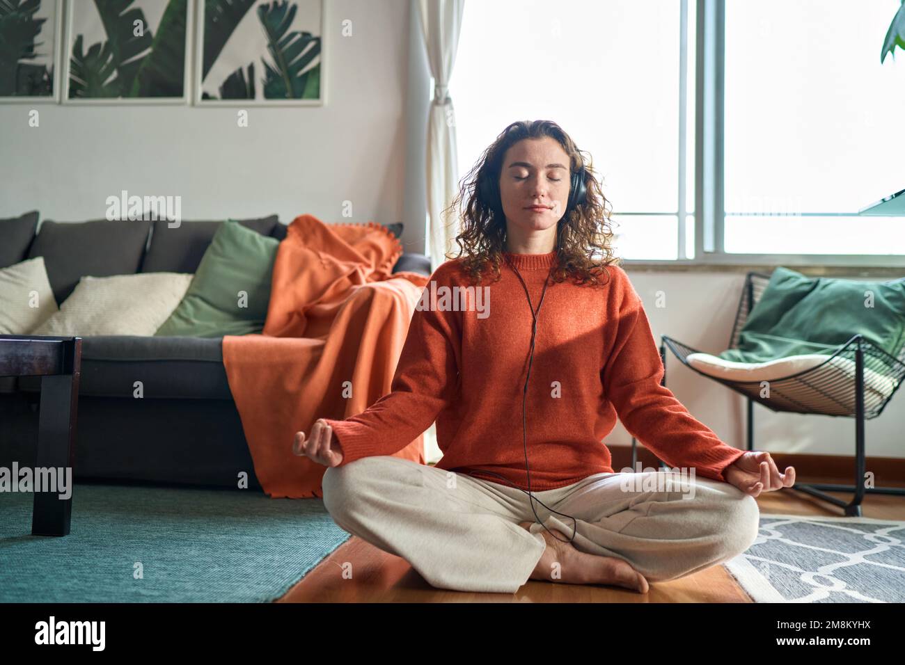 Jeune femme calme portant des écouteurs faisant de la méditation de yoga à la maison. Banque D'Images