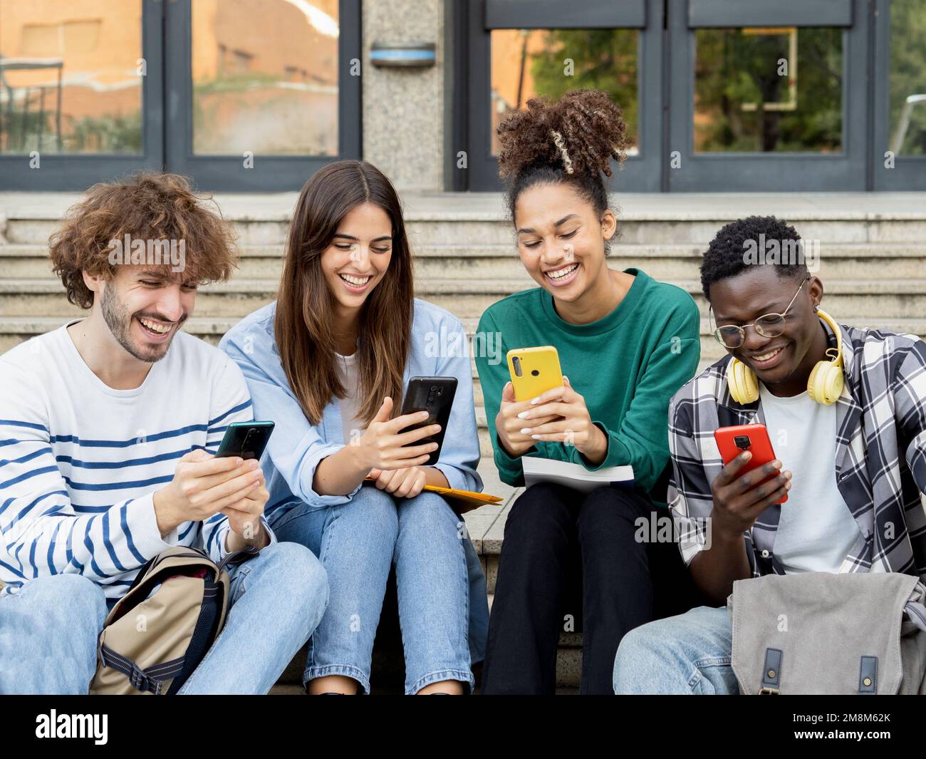 Groupe d'étudiants souriants et divers naviguent sur les réseaux sociaux avec des smartphones. Concept de médias sociaux Banque D'Images