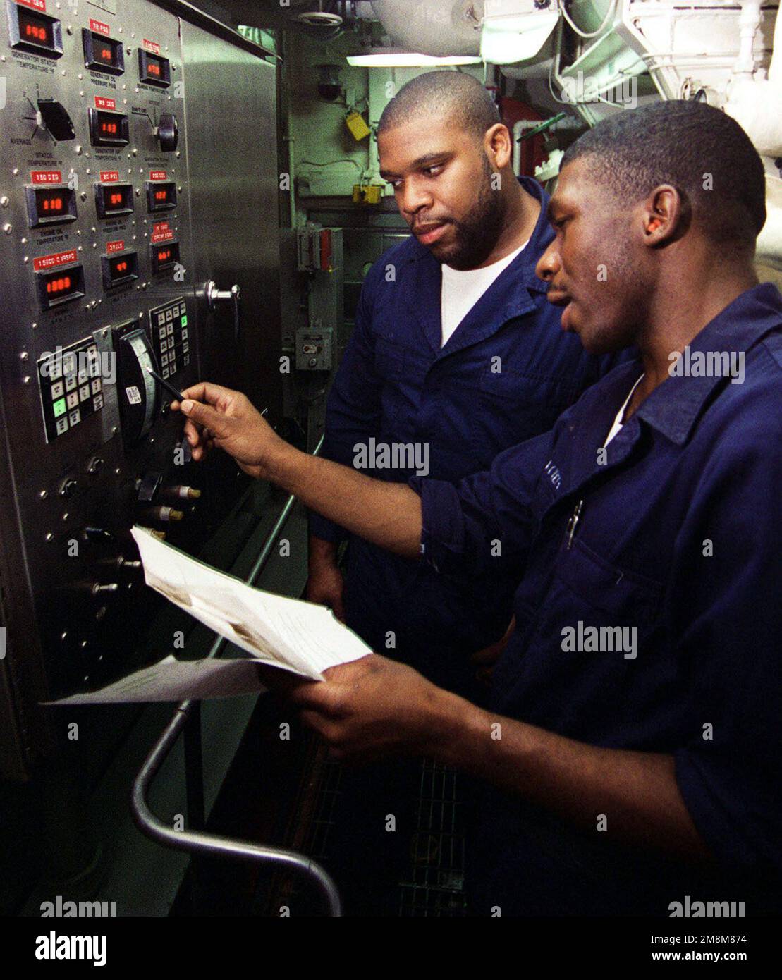 KEVIN Haigler, technicien en systèmes de turbines à gaz DE la marine AMÉRICAINE, forme le combattant américain Mate Fireman Chris Dawson sur le panneau de commande du générateur dans la salle principale des machines n° 1, à bord du croiseur de missiles guidé de classe Ticonderoga USS ANZIO (CG 68) de la marine américaine. Anzio participe à l'équipe d'évaluation de l'identification du combat de tous les services (ASCIET '96) au large de la côte de Gulfport, Mississippi. Base : USS Anzio (CG 68) Banque D'Images