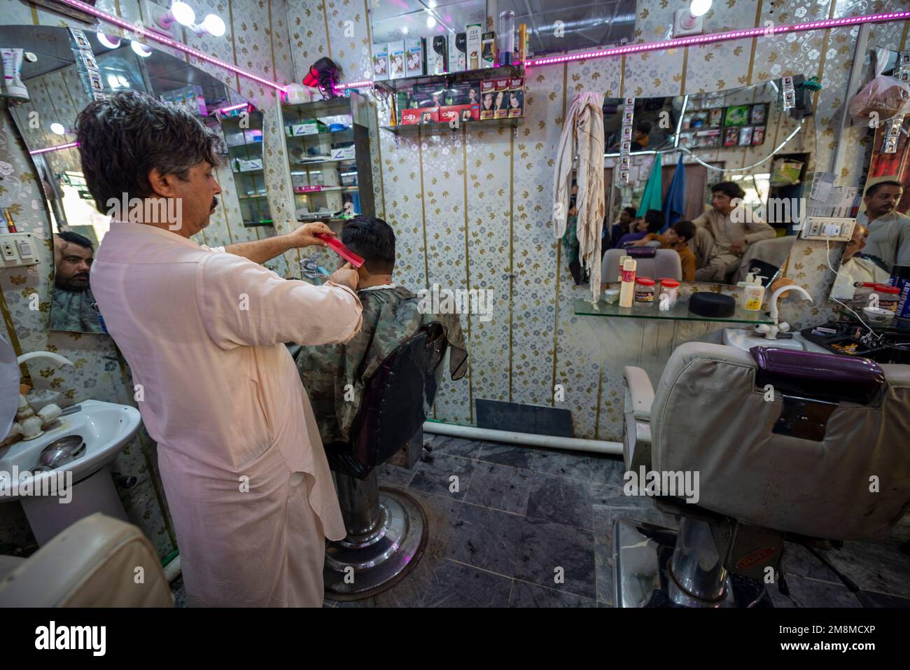 Barbier au service d'un client dans son salon de coiffure, Peshawar, Pakistan Banque D'Images