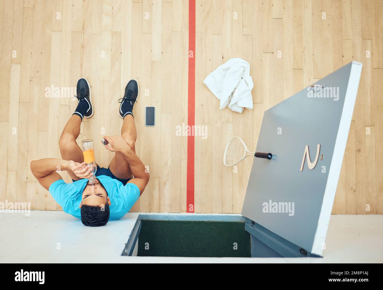 Au-dessus de la vue d'un jeune joueur de squash sportif assis seul et buvant de l'eau après avoir joué sur le terrain. Faites équipe avec un athlète de course mixte actif qui se repose Banque D'Images