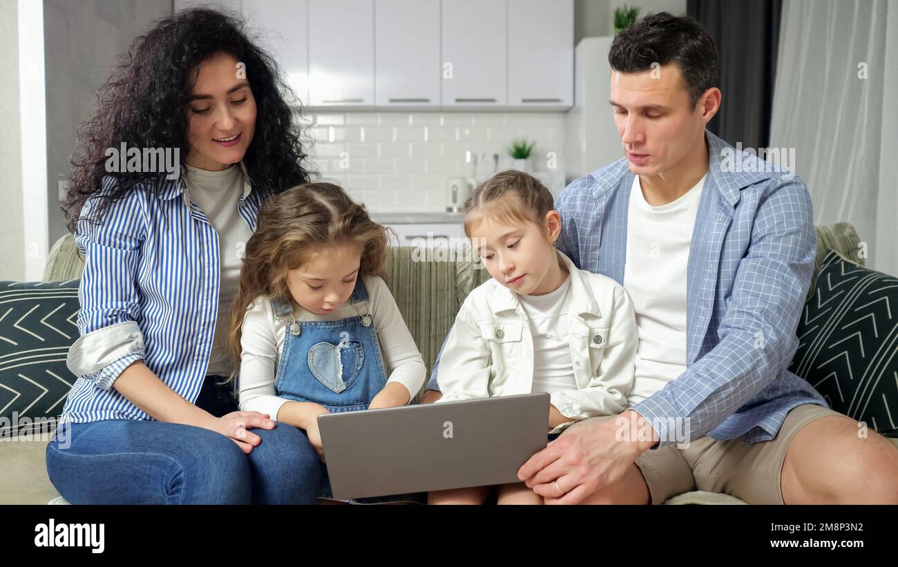 Des parents attentifs regardent des frères et sœurs enthousiastes jouer sur un ordinateur portable Banque D'Images