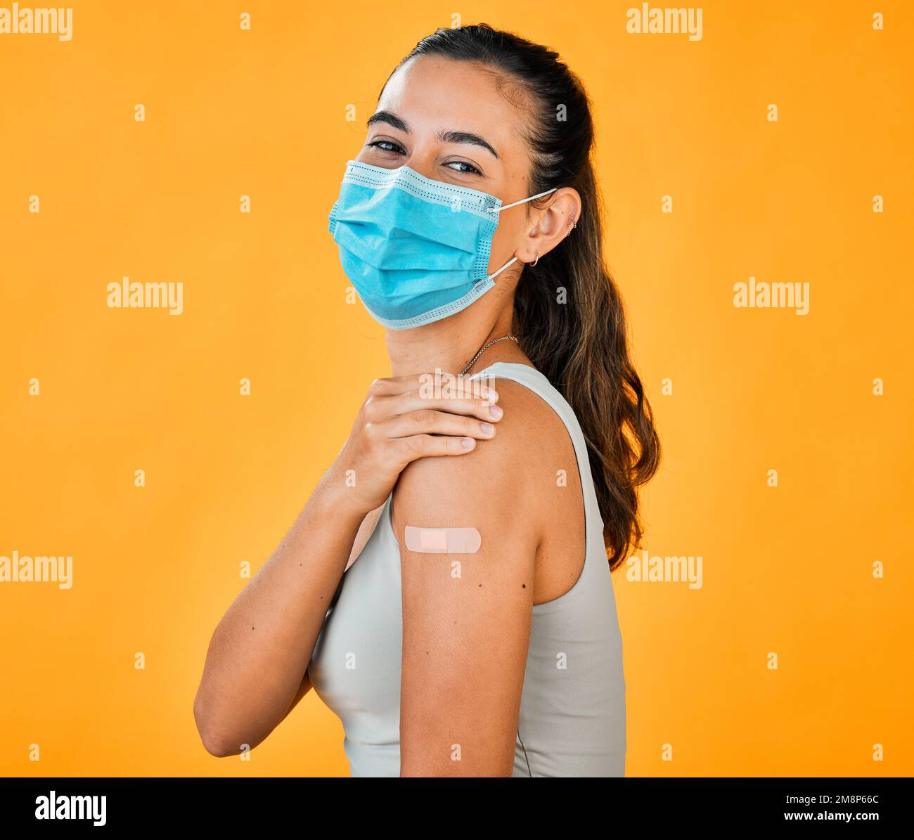 Race mixte Covid vaccinée femme montrant du plâtre sur le bras, portant un masque chirurgical. Portrait d'une femme hispanique isolée contre un studio jaune Banque D'Images