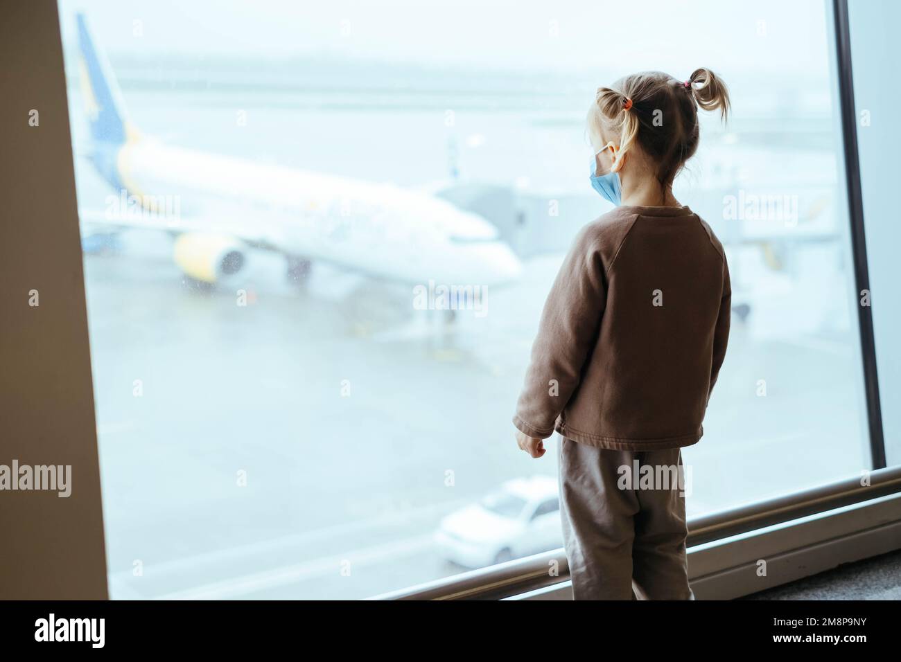 Enfant avec sac à dos regardant par la fenêtre de l'aéroport à l'avion.Voyage sûr avec les enfants pendant l'épidémie de Covid dans le masque facial. Passager enfant à l'arrivée Banque D'Images