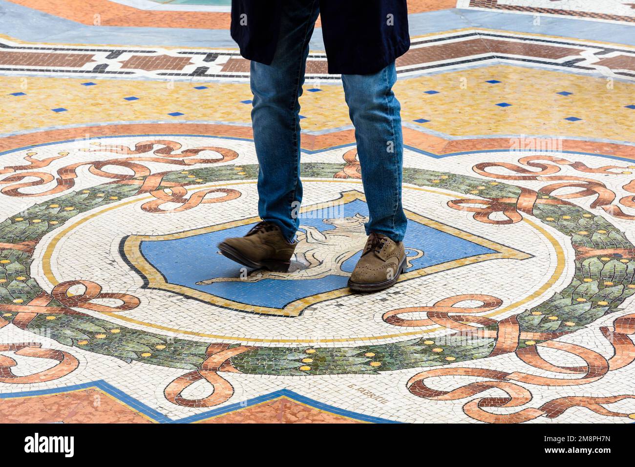 Un touriste faisant le rituel chanceux en tournant sur son talon sur les testicules du taureau dans une mosaïque dans la galerie Vittorio Emanuele II à Milan, Italie. Banque D'Images