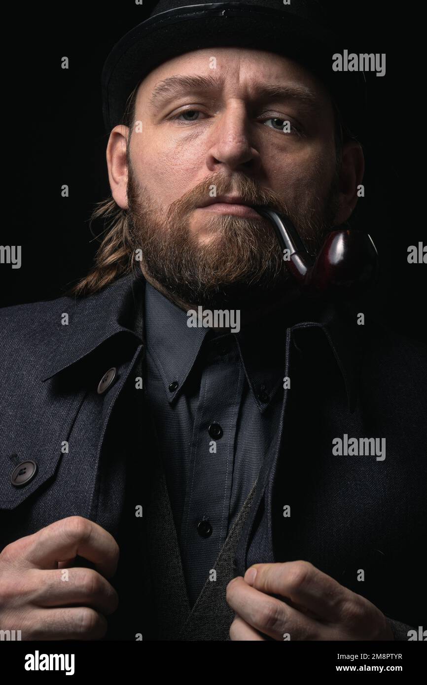 Homme élégant dans une tenue rétro costume chapeau fumeur pipe en bois sherlock holmes look cosplay angleterre gentleman tendance confient gangster Guy Ritchie Cha Banque D'Images