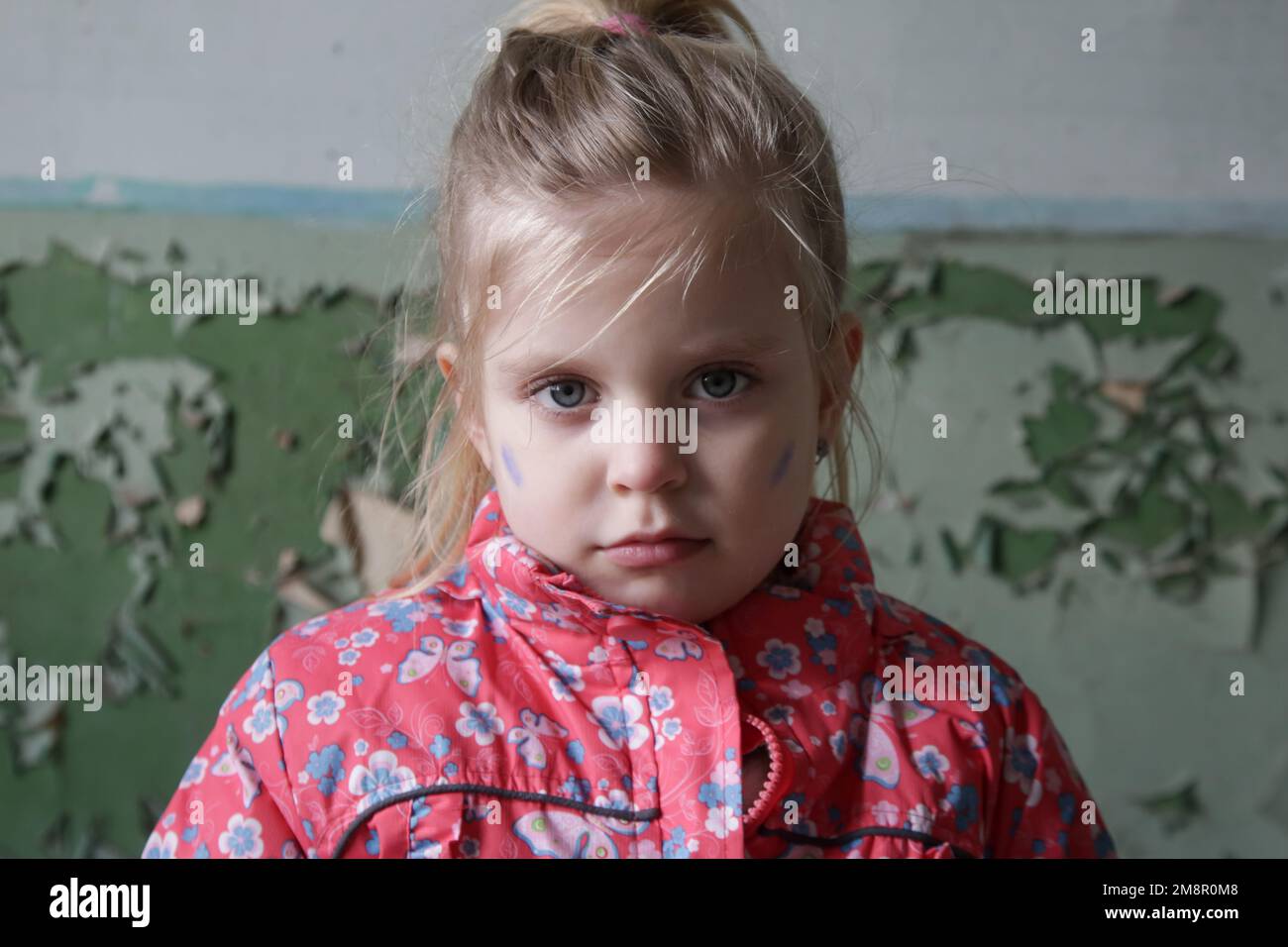 Portrait d'une petite fille dans un bâtiment en ruines avec drapeau d'Ukraine peint sur son visage. Réfugiés, crise de guerre, catastrophe humanitaire concept. Banque D'Images
