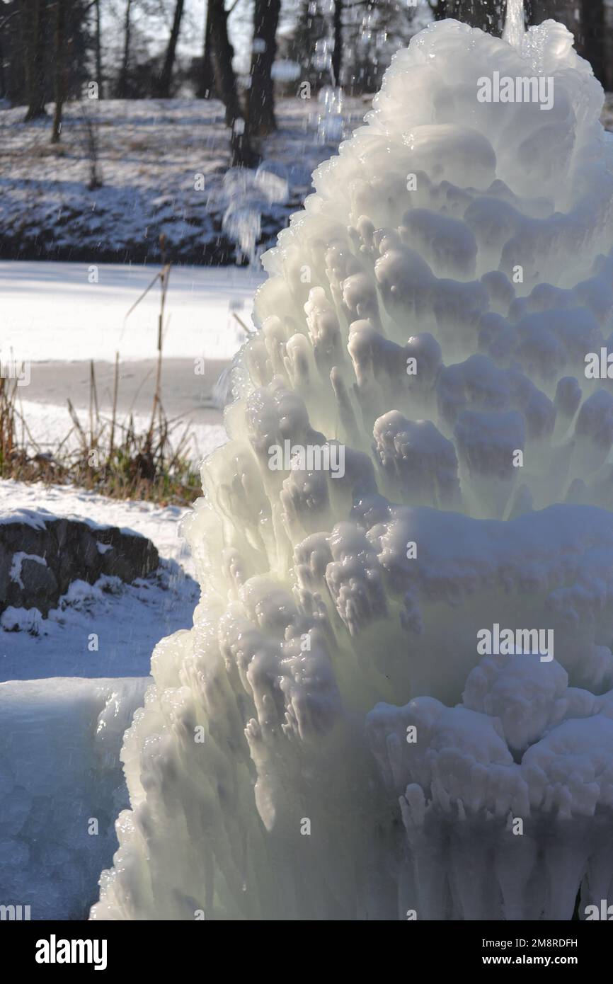 Fontaine glacée dans le parc par une journée ensoleillée en hiver. Fontaine avec eau gelée. Un jet d'eau d'une fontaine qui a glacé dans le froid. Arrière-plan couvert de glace et de neige dans le parc le jour Banque D'Images