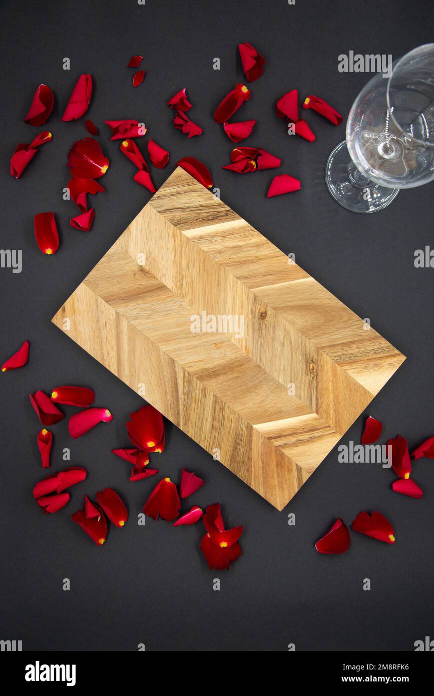 Planche à découper en bois pour cuisiner sur fond noir foncé avec un verre de vin et des pétales de rose rouge. Vue du dessus. Banque D'Images