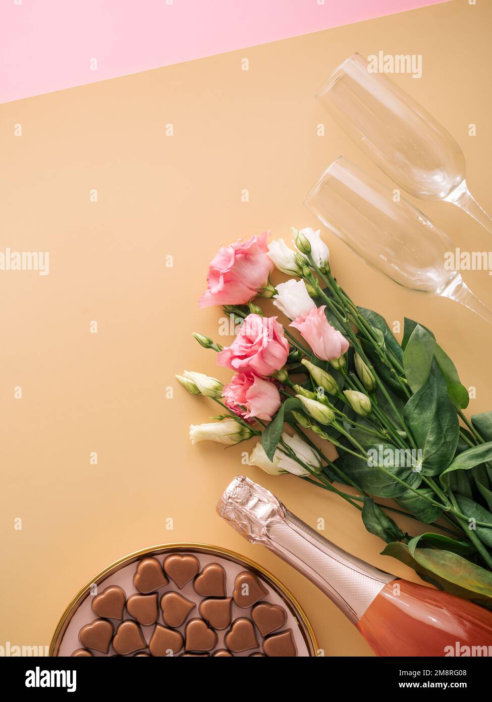 Concept de la Saint-Valentin sur fond jaune pastel. Bouteille de champagne rose, verres, bouqet de fleurs et confiseries romantiques au chocolat en forme de coeur.CopySpace.fond beige Champagne.Topview platlay Banque D'Images