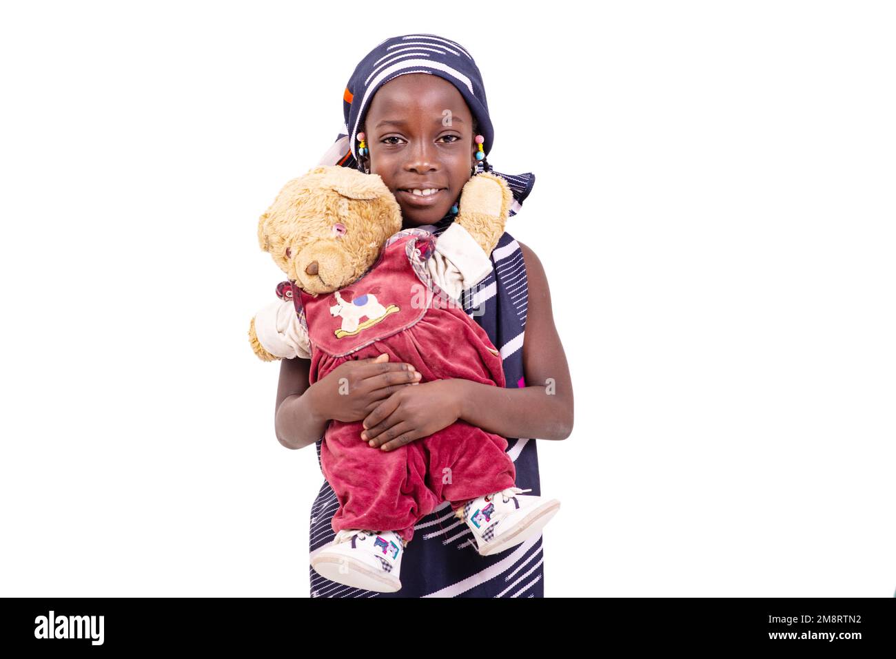 jolie petite fille portant un chiffon africain traditionnel et tenant son ours en peluche souriant. Banque D'Images