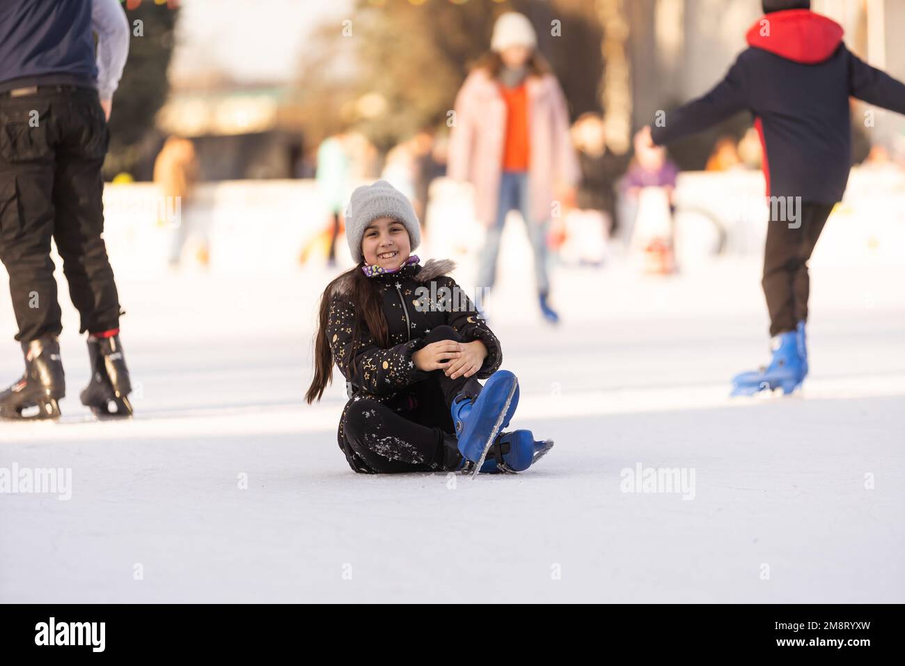 Une fille est tombée à la patinoire en hiver. la fille s'assoit sur la glace en patins, après une chute. Banque D'Images