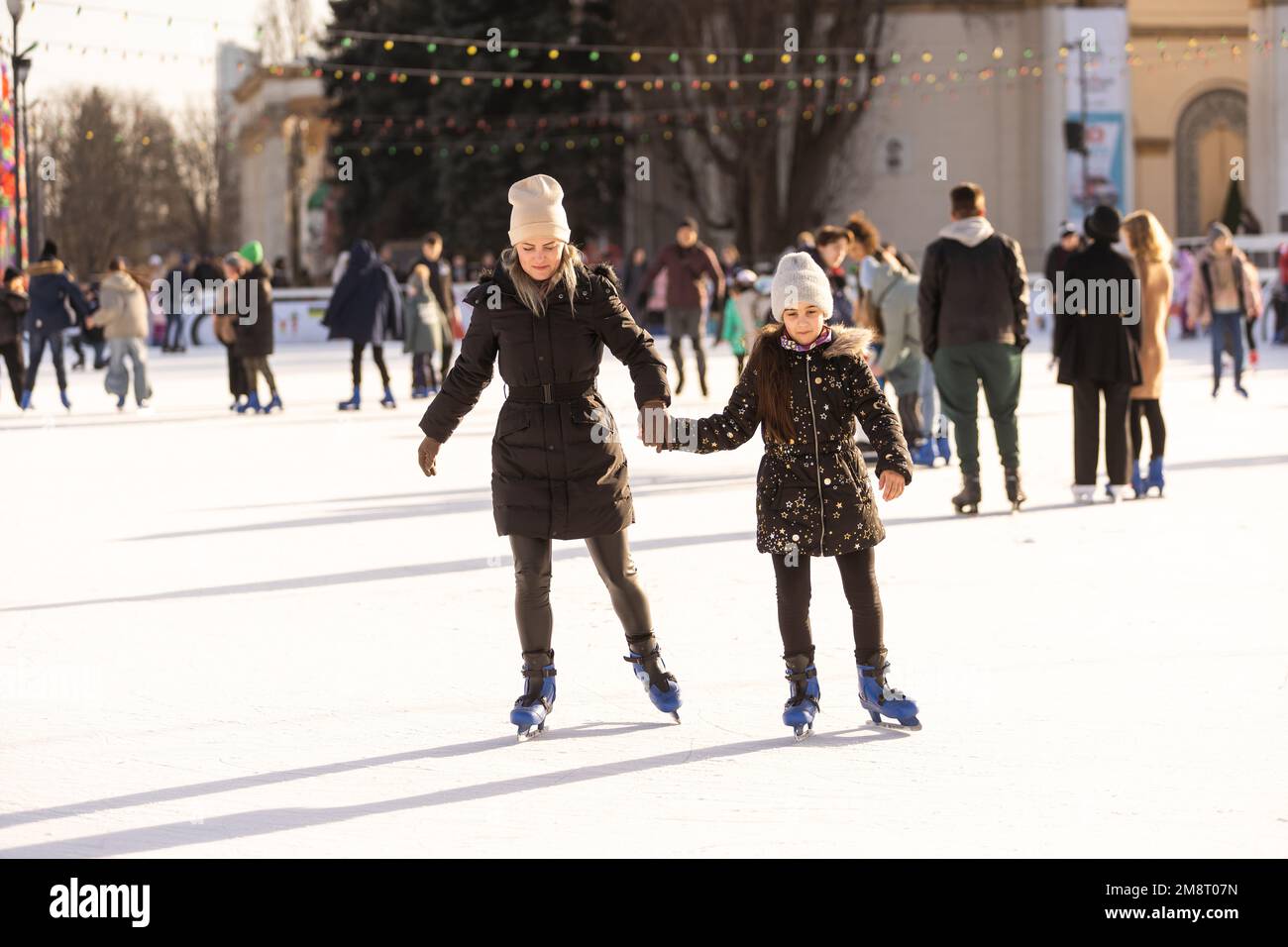 Photo d'action d'une belle femme enseignant à sa fille comment skate sur glace Banque D'Images