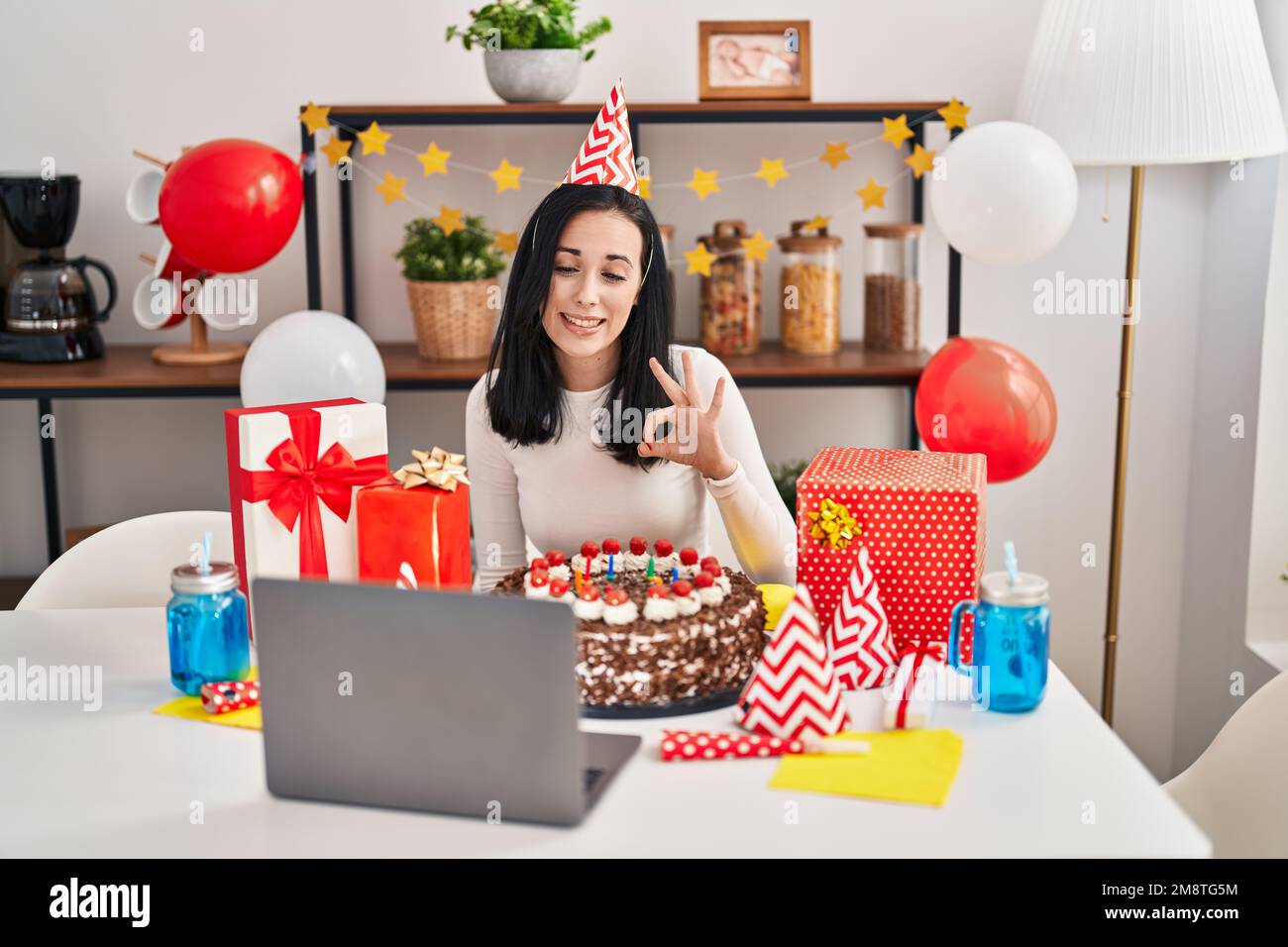 Femme hispanique célébrant l'anniversaire avec un grand gâteau au chocolat faisant appel vidéo faisant signe ok avec les doigts, souriant sympathique gestant excellent symbole Banque D'Images
