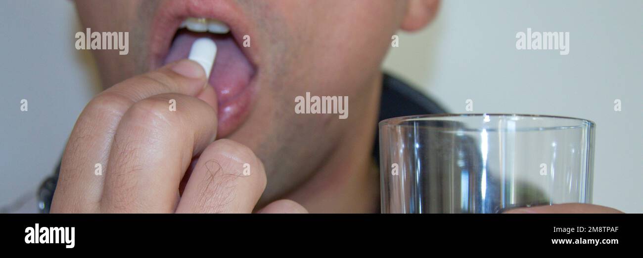 les mains d'un homme portant une pilule dans sa bouche et tenant un verre d'eau dans l'autre main. Effets secondaires des médicaments psychiatriques et divers médicaments. Banque D'Images
