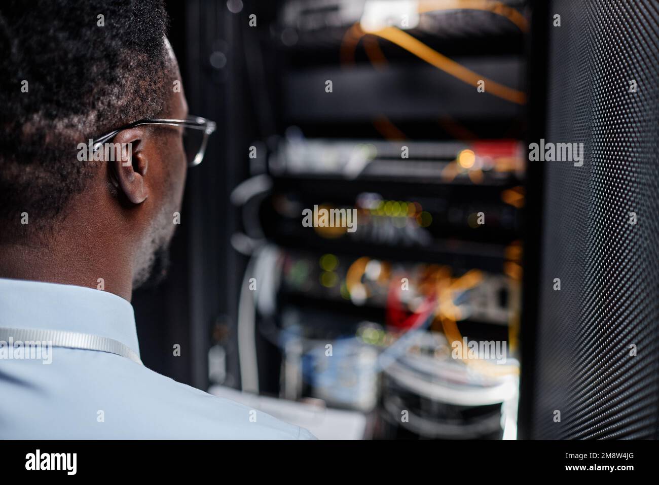 Vue arrière de l'ingénieur système noir travaillant avec l'armoire de serveur dans le centre de données, espace de copie Banque D'Images