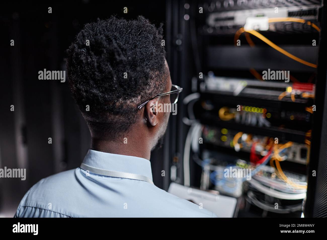 Vue arrière de l'homme noir en tant qu'ingénieur réseau travaillant avec l'armoire de serveur dans le centre de données, espace de copie Banque D'Images