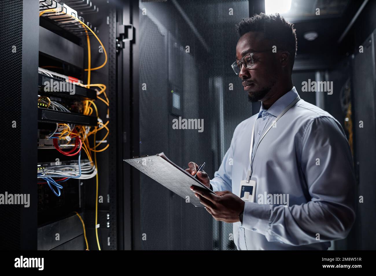 Vue de la taille vers le haut portrait d'un ingénieur réseau travaillant avec l'armoire de serveur dans le centre de données et prenant des notes sur le presse-papiers, l'espace de copie Banque D'Images
