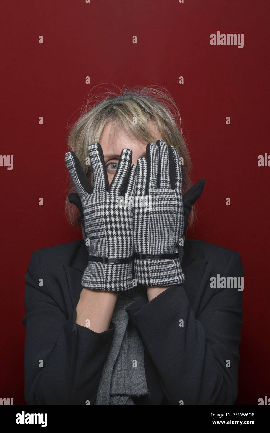 Tournez un œil aveugle. Une femme en gants élégants regarde la caméra avec ses doigts. portrait sur fond rouge Banque D'Images