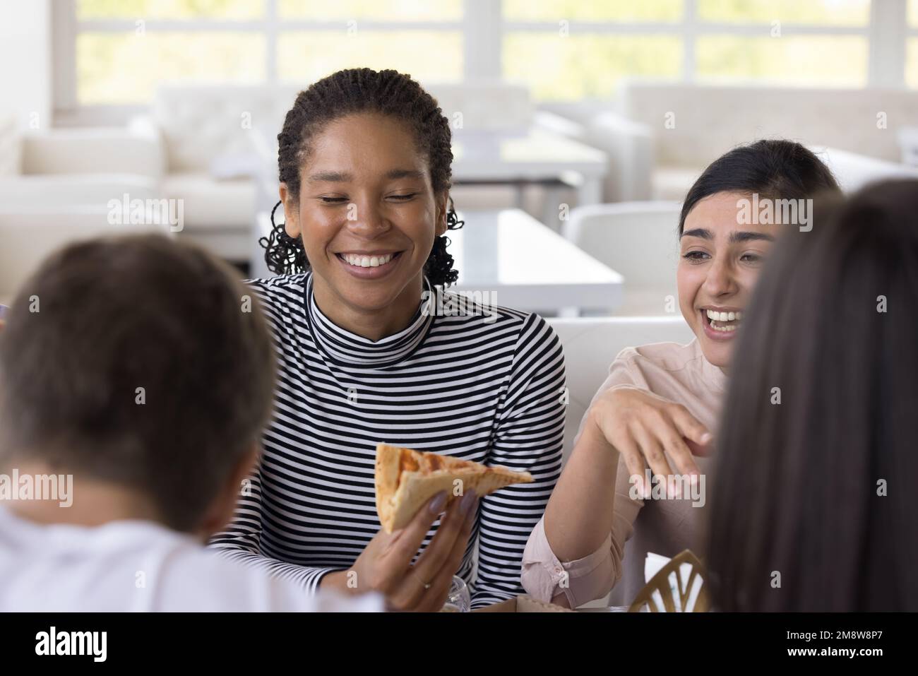 Des filles multiethniques gaies bavardent et rient, mangeant de la pizza dans la pizzeria Banque D'Images