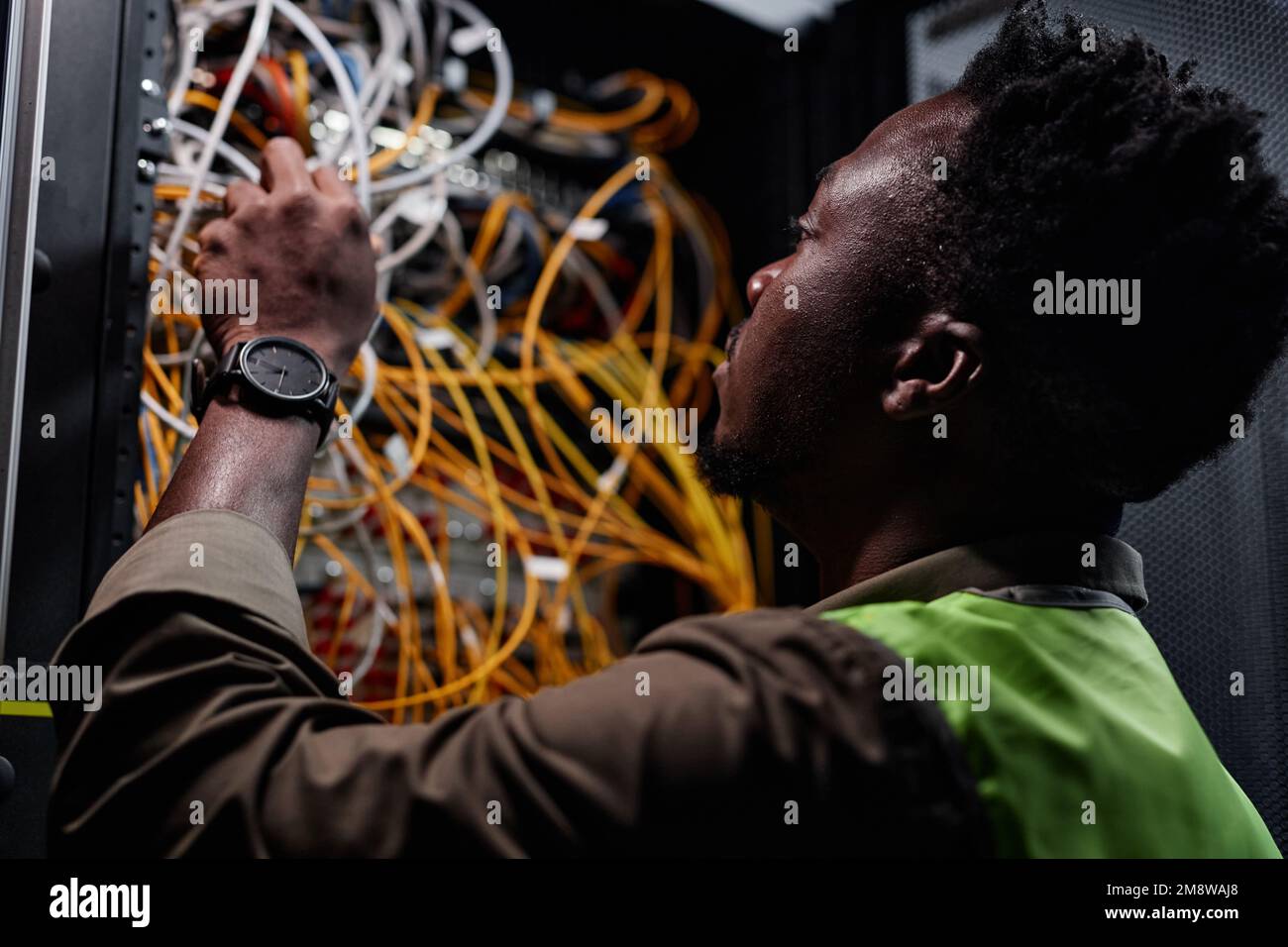 Gros plan de l'homme noir en tant que technicien réseau connectant les câbles et les fils lors de la réparation du serveur dans le centre de données Banque D'Images