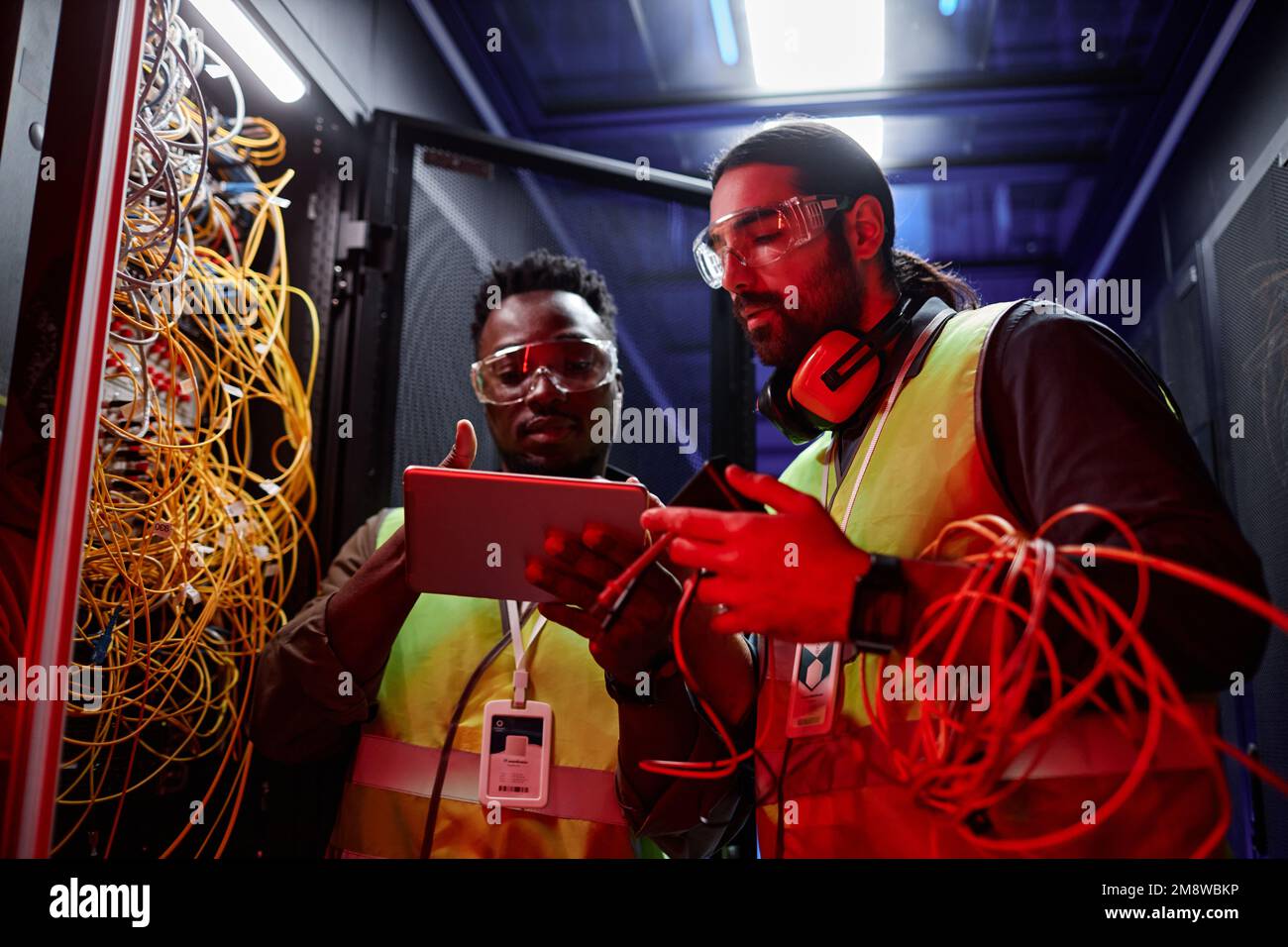Portrait de deux techniciens utilisant une tablette numérique lors de la réparation de serveurs et de la configuration d'un réseau de données sous un éclairage au néon Banque D'Images