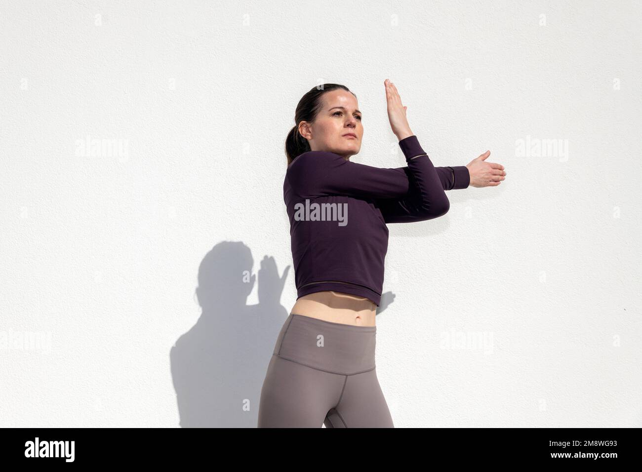 fit sportive femme faisant un effort d'étirement de bras exercice d'échauffement à l'extérieur contre un mur blanc. Banque D'Images