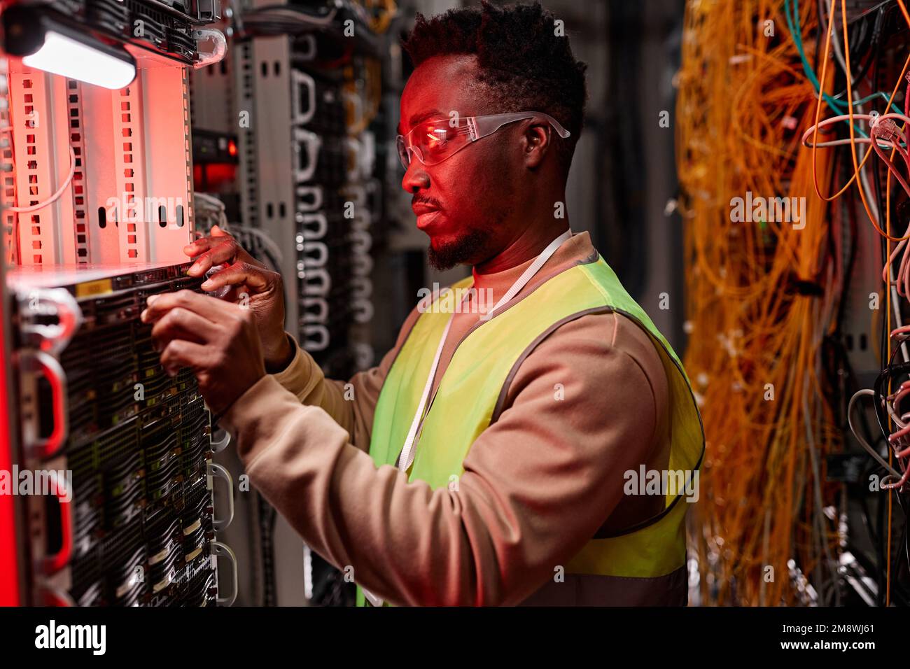 Vue latérale d'un technicien réseau inspectant les serveurs du centre de données, éclairé par une lumière néon rouge Banque D'Images