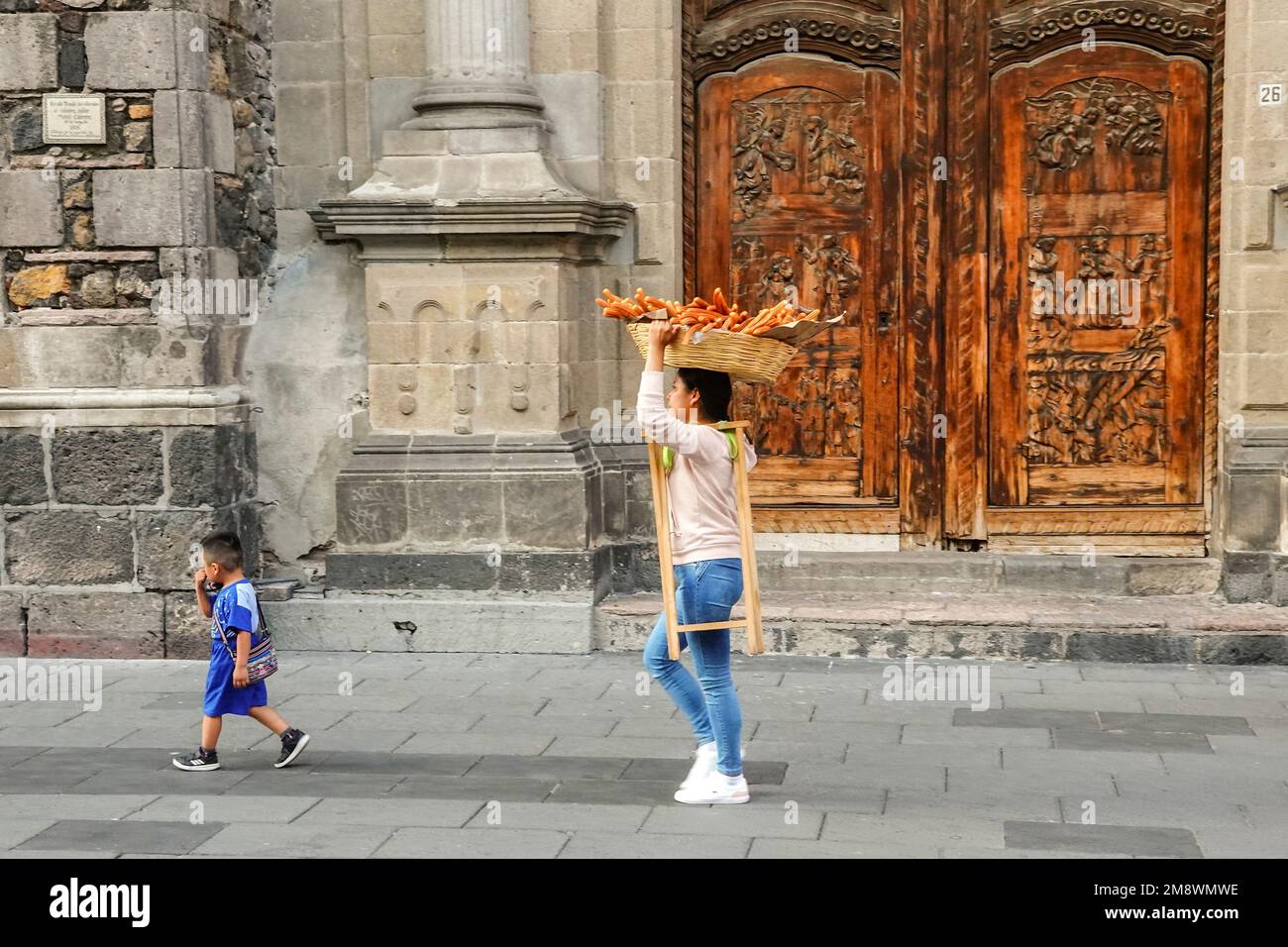 Un marchand d'enfants et de churros passe devant les portes en bois sculpté de l'église Templo de Santa Inés et de l'ancien couvent dans le quartier Zona Centro de Mexico, au Mexique. Banque D'Images